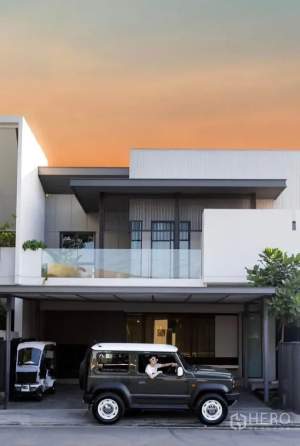 Townhouse for rent or sale in Bang Phli, Samut Prakan - Modern two-storey townhouse facade with glass balcony and covered multi-car parking at sunset.