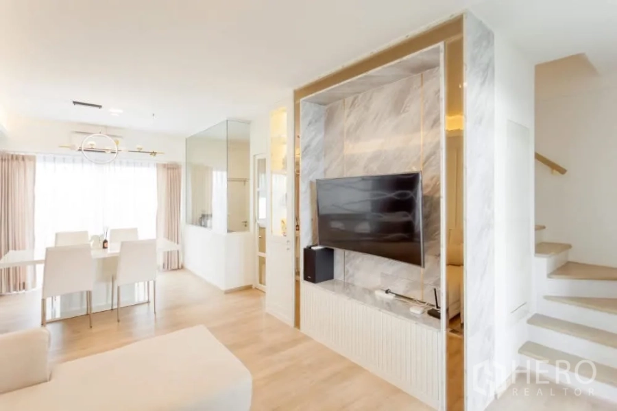 Townhouse for rent in Prawet, Bangkok - Marble-accent TV wall and media cabinet next to a bright staircase in the living area.