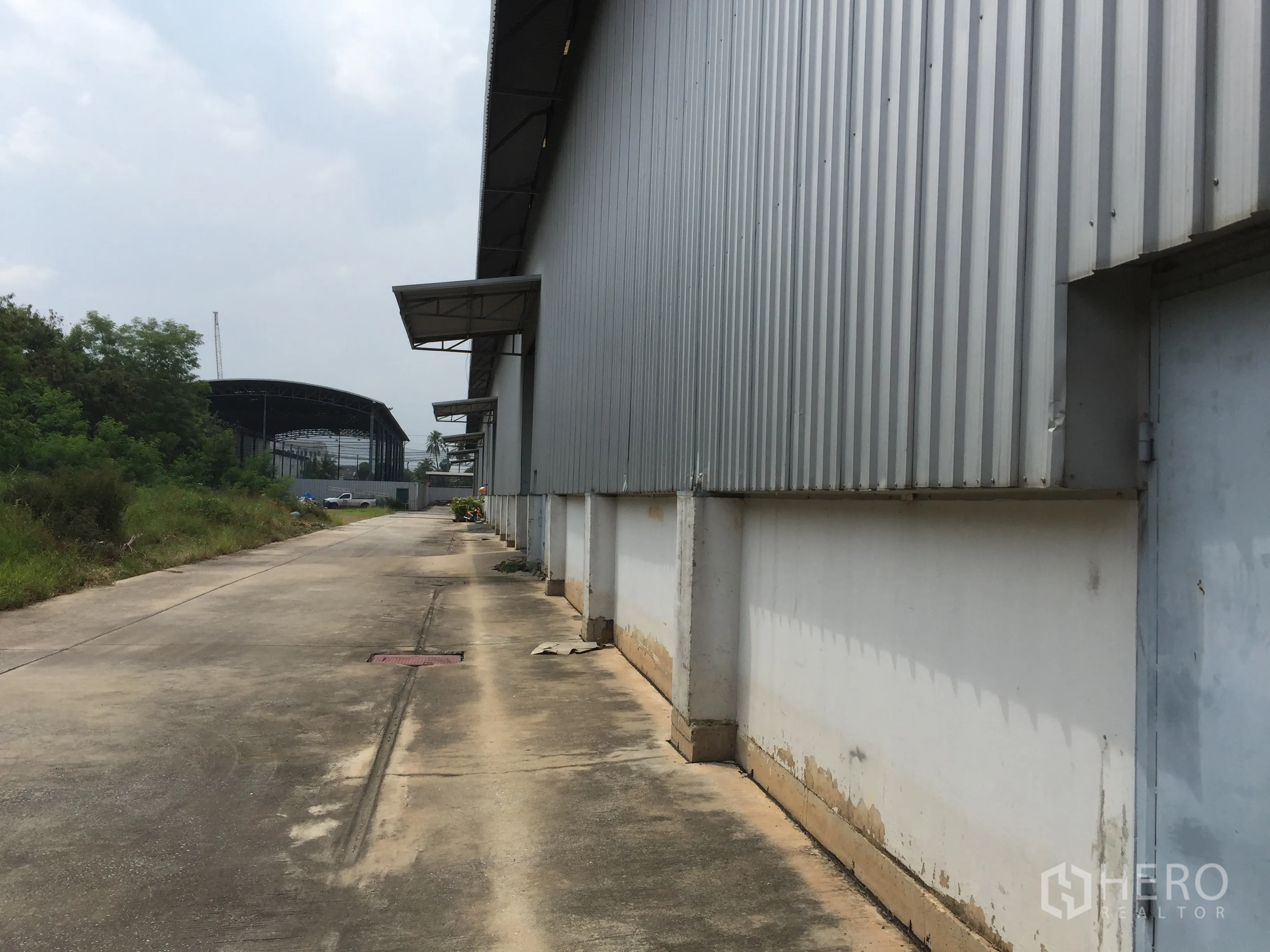 Factory for rent in Khlong Luang, Pathum Thani - Service road running along the corrugated metal exterior of the factory.