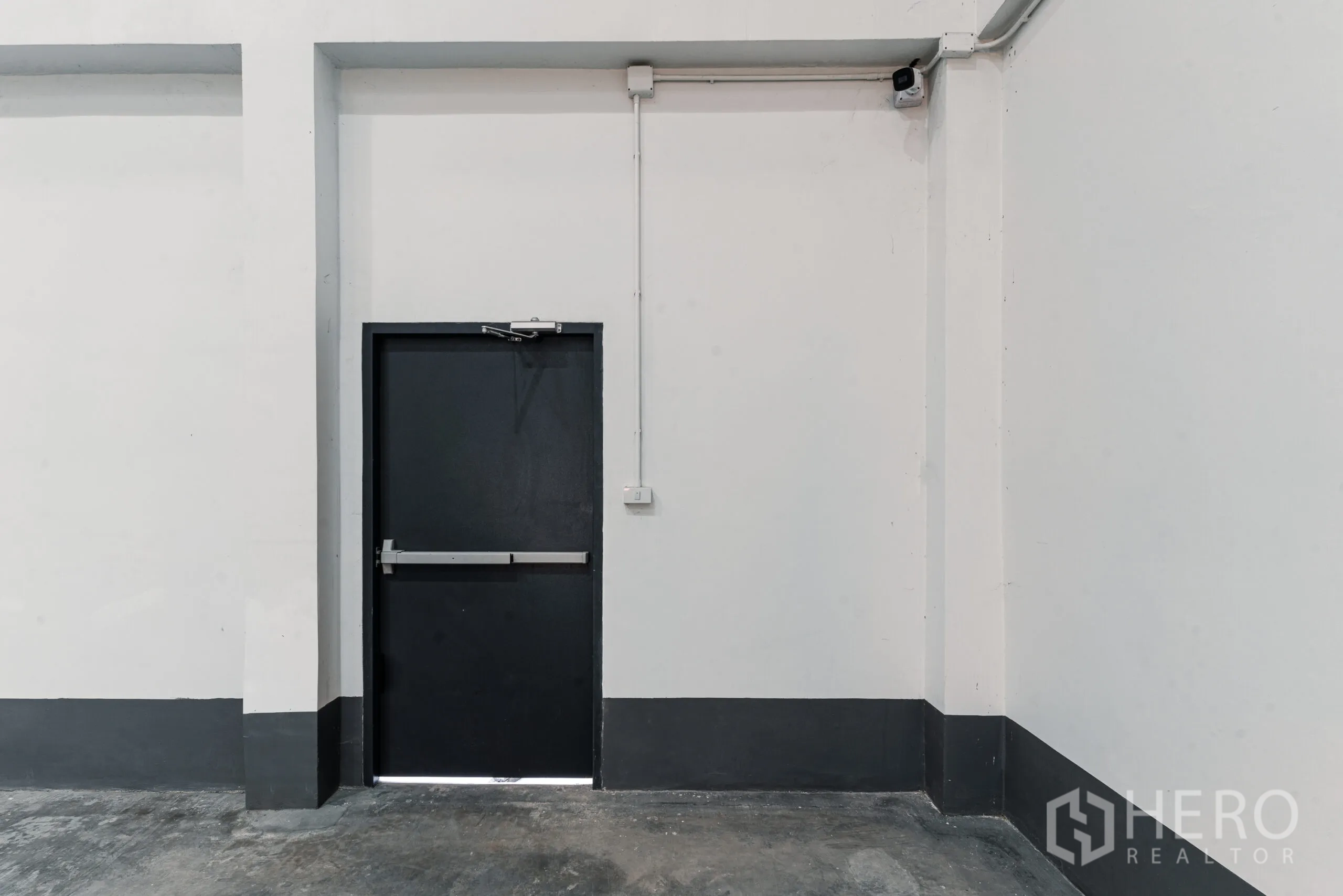 Warehouse for rent in Mueang Samut Sakhon, Samut Sakhon - Close-up of a steel emergency exit door with CCTV camera on a clean interior wall.
