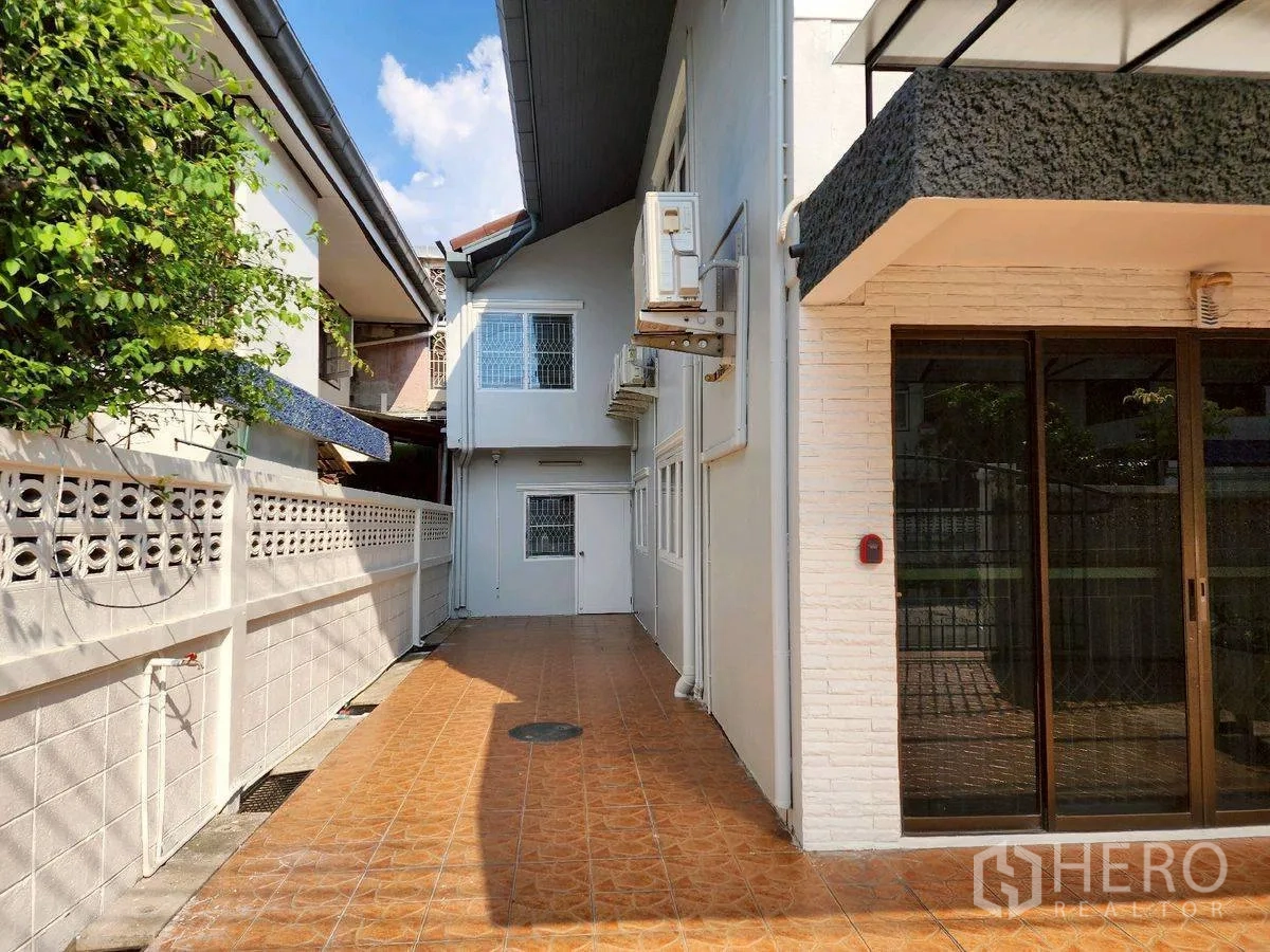Detached House for rent in Huai Khwang, Bangkok - Side exterior with tiled walkway and white walls along the boundary fence.