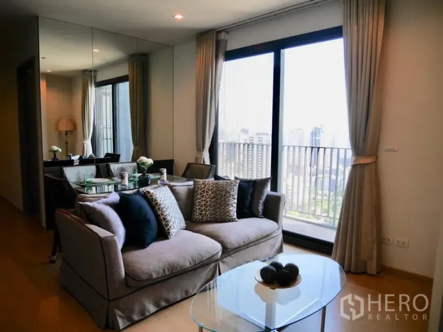 Condominium for rent in Watthana, Bangkok - Bright living room with sofa, glass coffee table, balcony doors and Bangkok skyline view in a Thonglor condo.