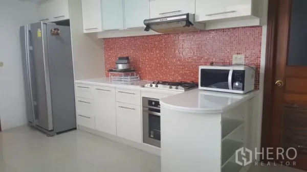 Condominium for rent in Khlong Toei, Bangkok - Modern white kitchen with gas hob, oven, and red mosaic tile backsplash.