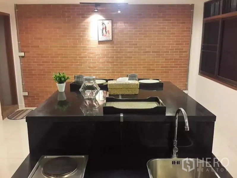Townhouse for rent in Khlong Toei, Bangkok - Kitchen island with glossy black countertop and sink set against a brick accent wall.
