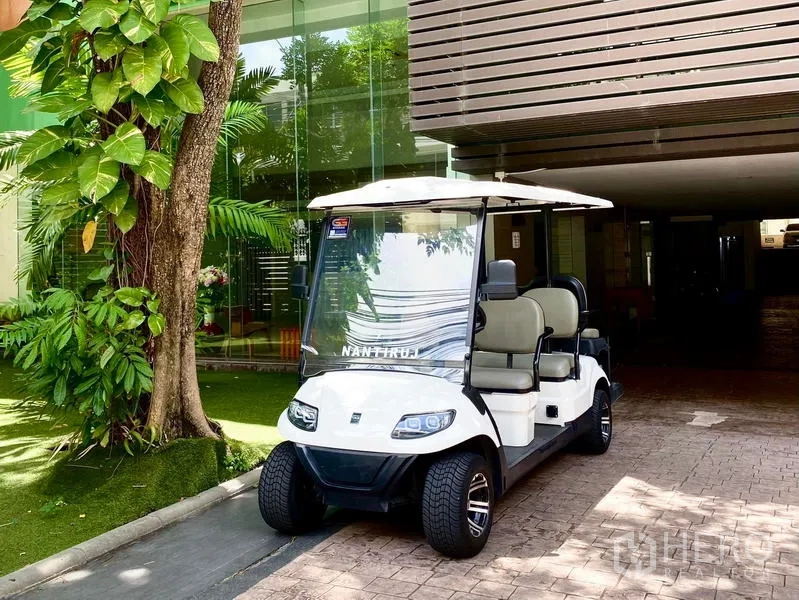 Condominium for rent in Khlong Toei, Bangkok - Resident shuttle golf cart parked at the condominium entrance amid greenery.