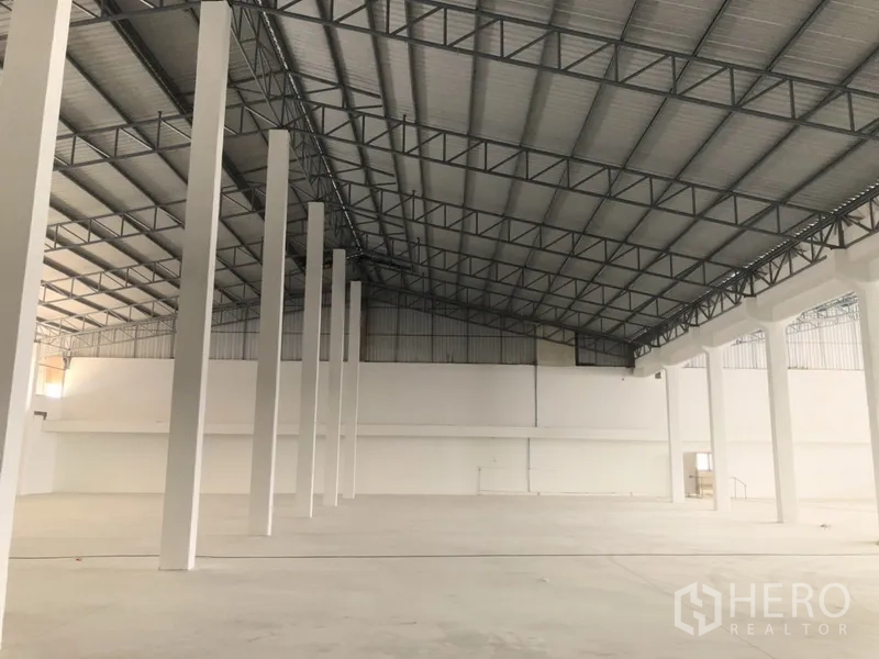Warehouse for rent in Nonthaburi - Bright warehouse hall with pitched metal roof, steel beams, and tall columns for clear stacking height.