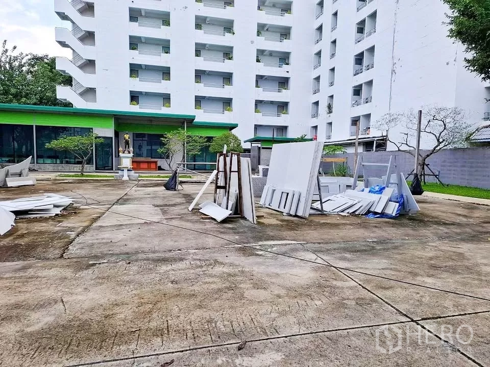 Warehouse for rent in Bang Kapi, Bangkok - Large open forecourt for loading and parking with landscaping and neighboring building in view.
