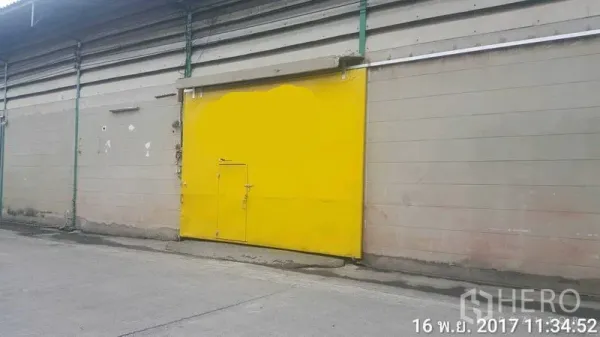 Factory for rent in Bang Phli, Samut Prakan - Factory exterior with large yellow sliding metal door along a concrete access road.