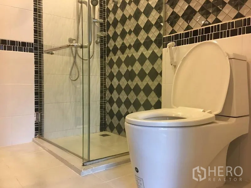 Townhouse for rent in Bang Rak, Bangkok - Modern bathroom with glass-enclosed shower, handheld shower and toilet, featuring diamond-pattern tiles.