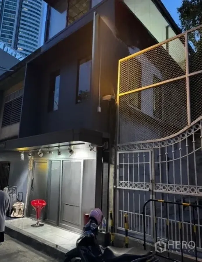 零售空间 出租在Khlong Toei, Bangkok - 两层深灰色商铺外立面，傍晚灯光与铁门可见