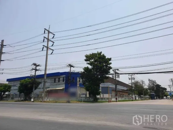 Factory for rent in Bang Pakong, Chachoengsao - Street view of the industrial complex on a main road with power lines, trees and a perimeter fence.