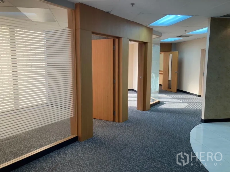 Office Space for rent - Hallway with glass partitions and wooden door frames leading to private offices under recessed lighting.