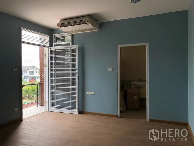 Detached House for sale in Bang Khen, Bangkok - Upstairs bedroom with wood floors, air conditioner, balcony access through glass door and ensuite entrance.