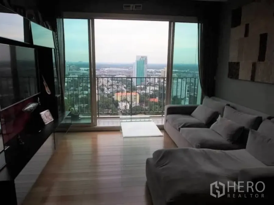 Condominium for rent in Khlong Toei, Bangkok - High-floor living room with floor-to-ceiling windows, balcony and sweeping Bangkok skyline view.