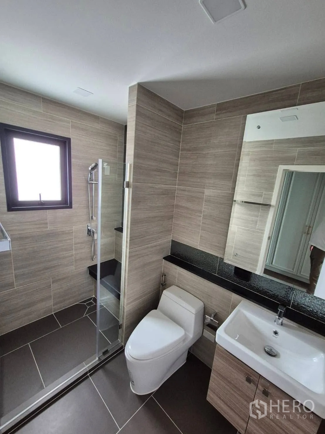 Detached House for sale in Bang Kruai, Nonthaburi - Modern bathroom with glass shower enclosure, vanity and toilet in wood‑tone tiles.