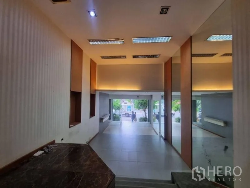 Shophouse for rent in Watthana, Bangkok - View from raised platform toward the glass entry, mirrors, and ceiling lights.