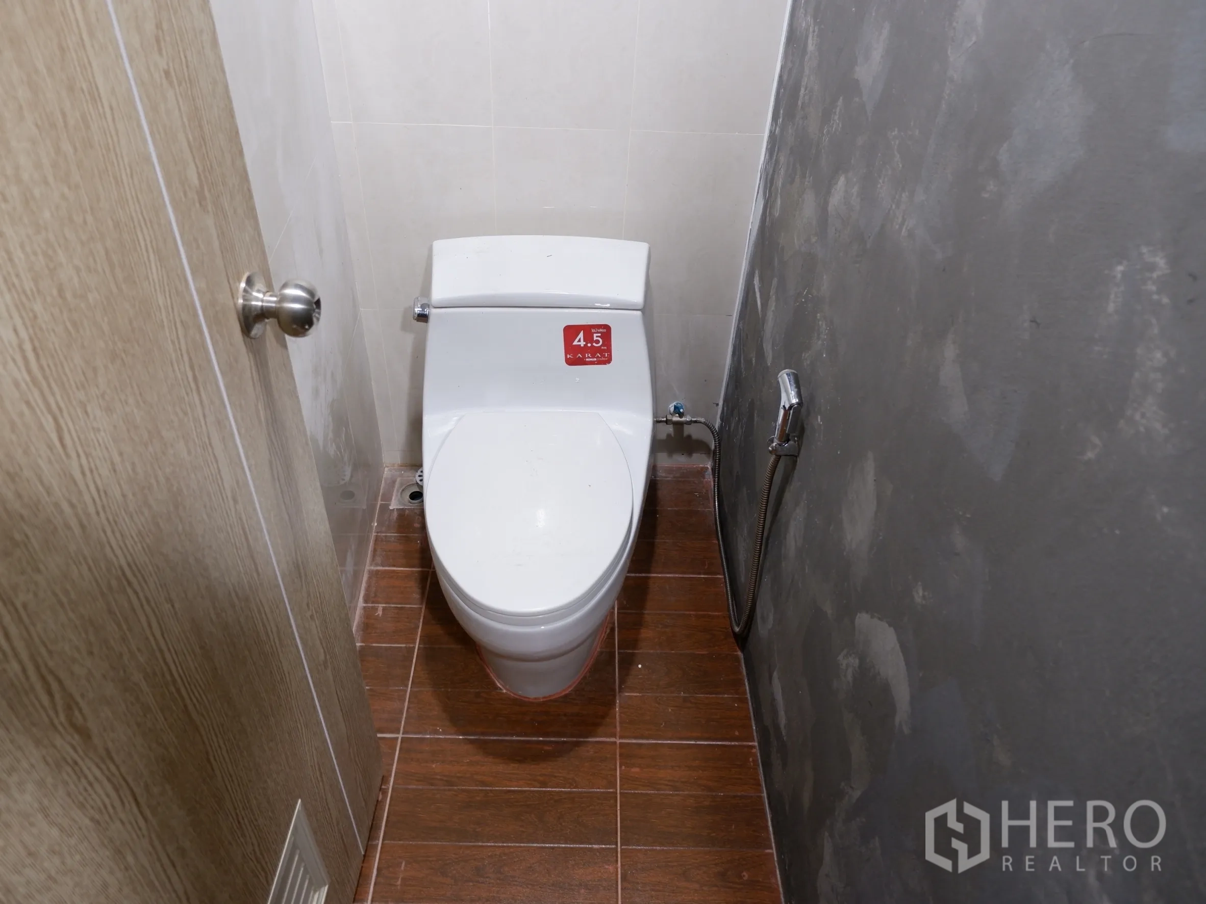 Home Office for sale in Bang Rak, Bangkok - Clean restroom featuring a white toilet, spray hose and wood-look tile floor.