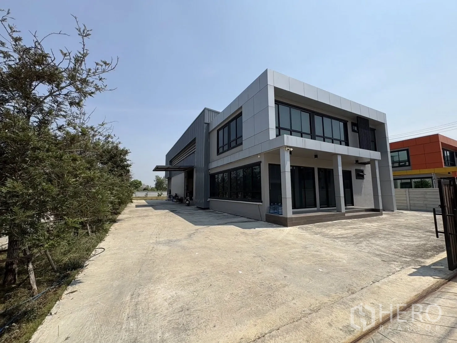 Factory for rent or sale in Bang Len, Nakhon Pathom - Angled view of the contemporary factory with glass windows and an expansive paved yard.