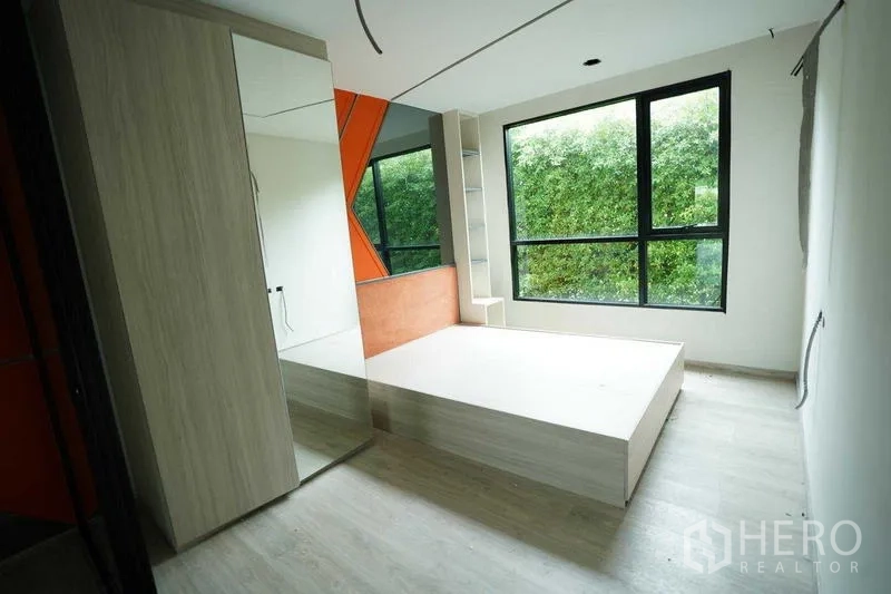 Standalone for rent in Bang Na, Bangkok - Bright room with platform bed and an orange feature wall beside a big window.