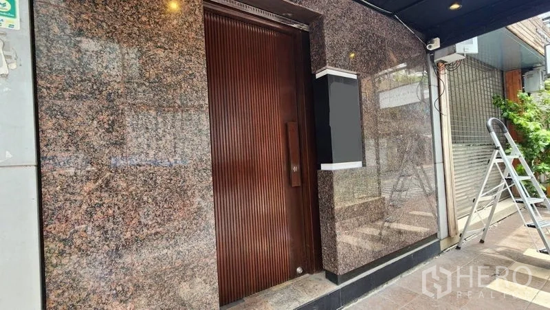 Shophouse for rent in Khlong Toei, Bangkok - Granite-clad main entrance with solid wood door and signage box at street level.