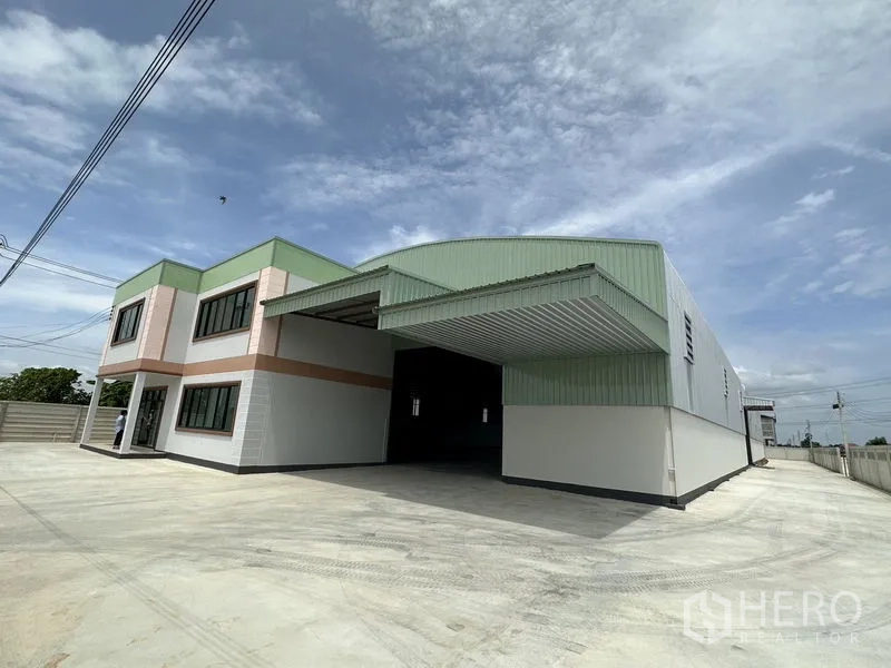 Factory for rent or sale in Sai Noi, Nonthaburi - Angled exterior view showing covered loading bay, large concrete yard and steel‑clad warehouse façade.
