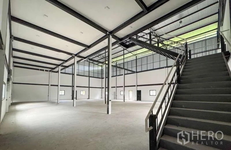 Warehouse for rent in Bang Phli, Samut Prakan - Wide warehouse floor with steel structure and stair access to mezzanine beneath a translucent roof strip.