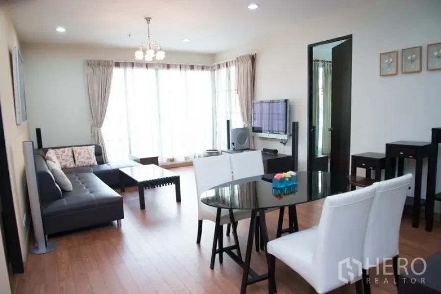Condominium for rent in Khlong Toei, Bangkok - Bright living and dining area with L-shaped leather sofa, glass table and floor-to-ceiling windows in a Sukhumvit condo.