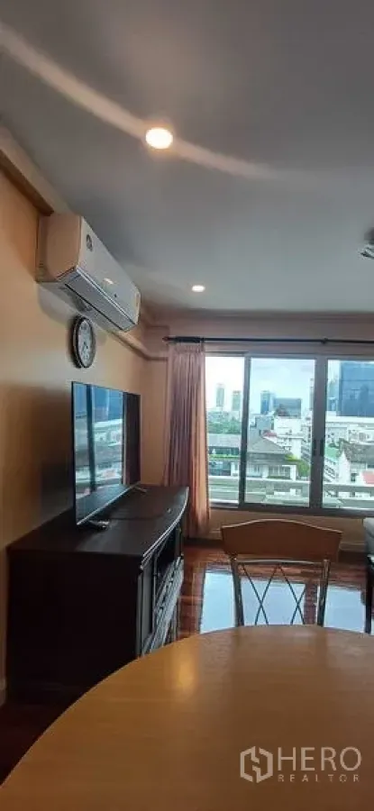Condominium for sale in Pathum Wan, Bangkok - Living room angle showing air conditioner, TV cabinet and wide windows overlooking the city.