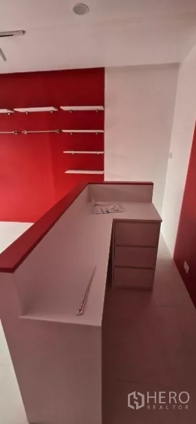 Retail Space for rent in Watthana, Bangkok - Close-up of L-shaped white cashier counter with drawers beside a red display wall and track lighting.