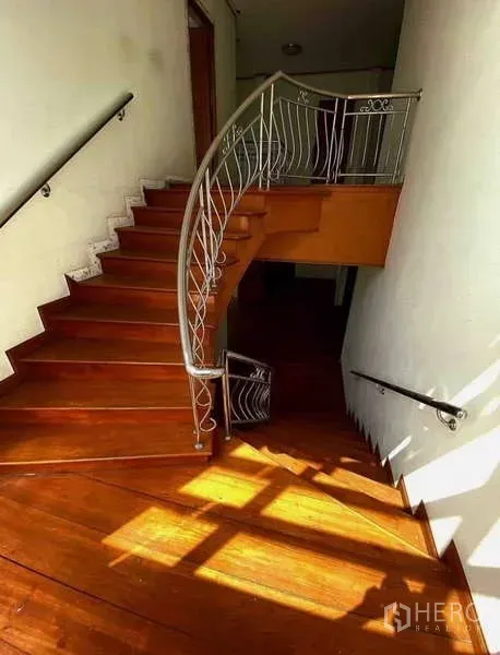 Detached House for sale in Prawet, Bangkok - Curved wooden staircase with a metal handrail lit by natural sunlight.