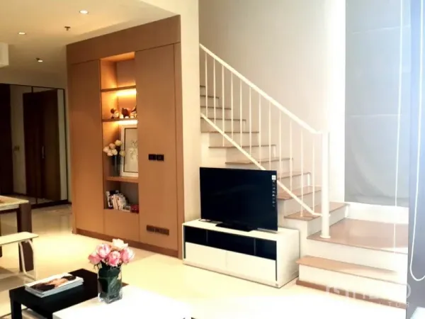 Condominium for rent in Khlong Toei, Bangkok - Bright duplex living area with TV console, built-in shelving and staircase.