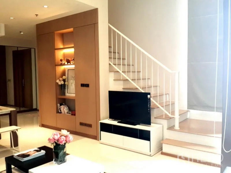 Condominium for rent in Khlong Toei, Bangkok - Bright duplex living area with TV console, built-in shelving and staircase.