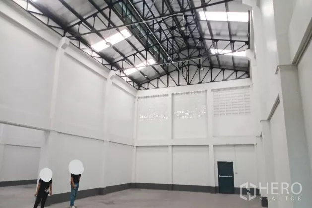 Warehouse for rent in Mueang Samut Sakhon, Samut Sakhon - Bright high-bay warehouse hall with steel truss roof, ventilation blocks and an emergency exit door.