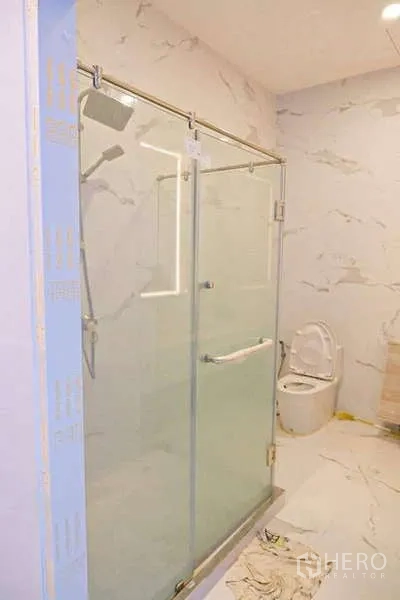 Detached House for sale in Lat Phrao, Bangkok - Light marble-pattern bathroom with glass shower enclosure and toilet.