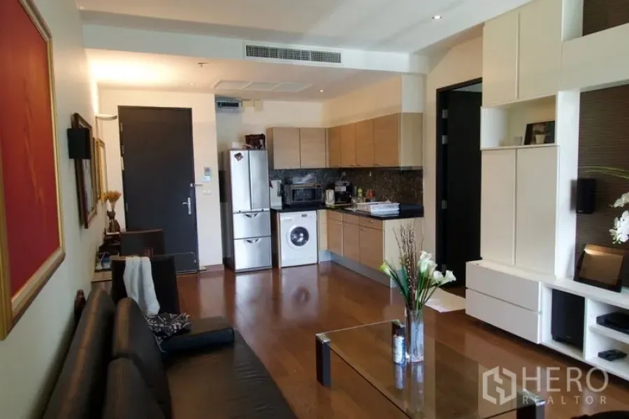 Condominium for sale in Pathum Wan, Bangkok - Open-plan living room with wooden floors, built-in shelving, and a kitchenette with fridge and washing machine.