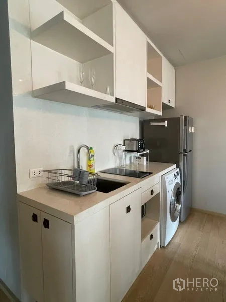 Condominium for rent in Bangkok - Linear kitchen with sink, cooktop, open shelving, refrigerator and washer.
