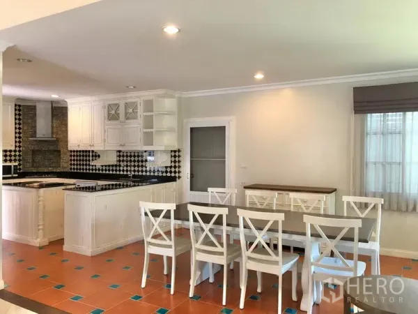 Detached House for rent in Mueang Samut Prakan, Samut Prakan - Dining space connected to kitchen with terracotta floor accents, long table and white chairs.