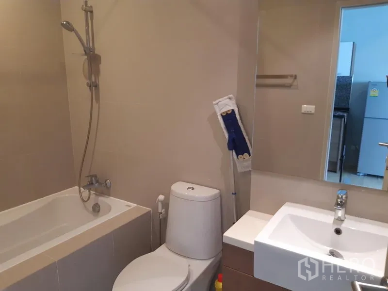 Condominium for rent in Bangkok - Modern bathroom featuring a bathtub-shower combo, toilet, and vanity with mirror.