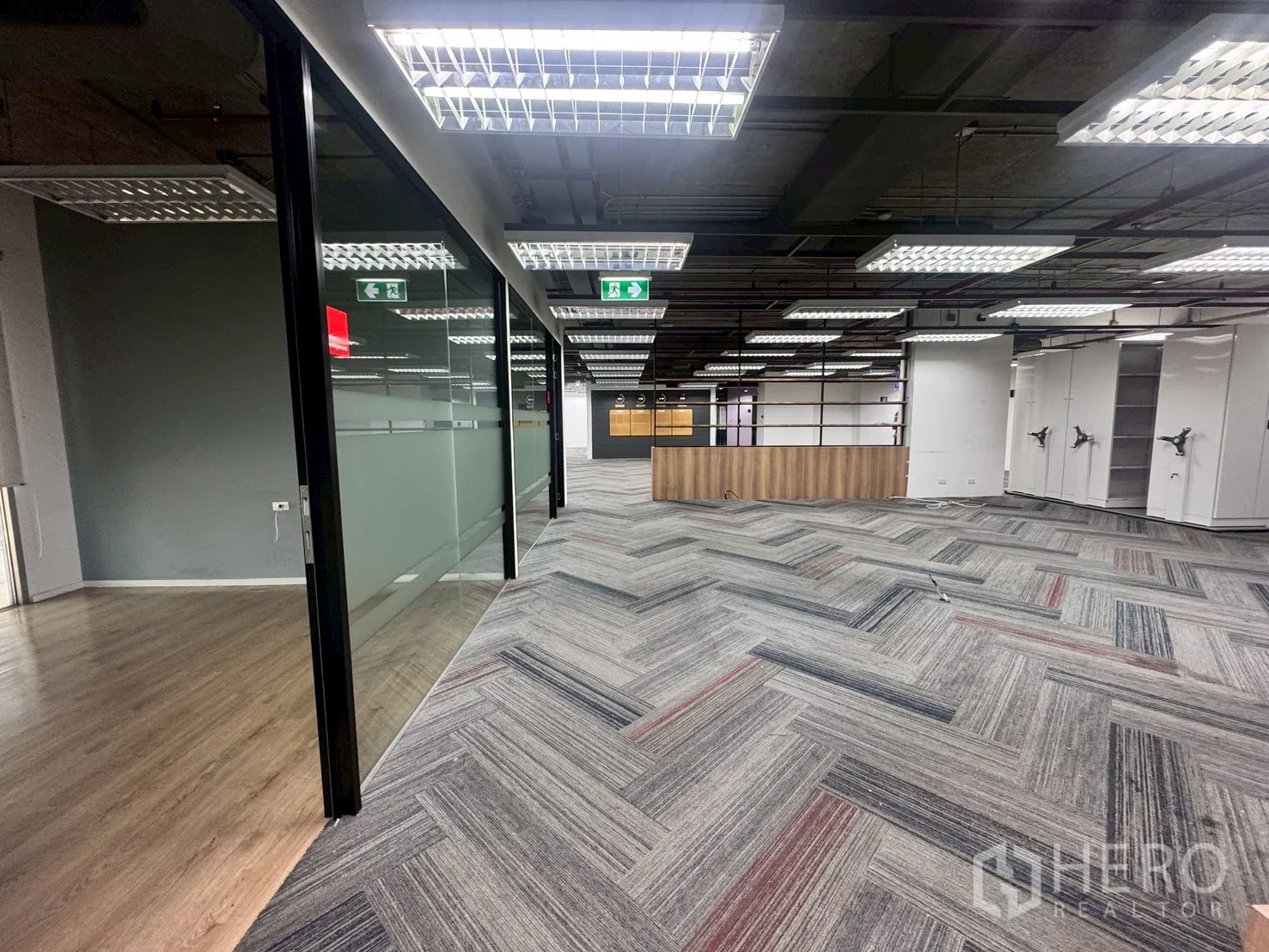 Office Space for rent in Watthana, Bangkok - Glass-partitioned corridor opening into an open-plan workspace with carpet tiles and lighting panels.