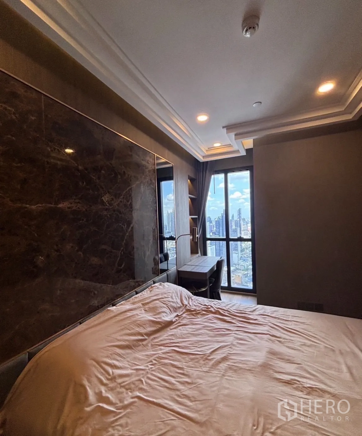 Condominium for rent in Bang Rak, Bangkok - Bedroom with a marble feature wall, built-in desk, and floor-to-ceiling window overlooking the city skyline.
