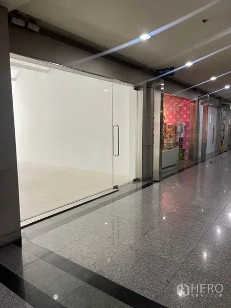 Retail Space for rent in Khlong Toei, Bangkok - Indoor mall corridor view of a vacant retail shop with full-height glass frontage.