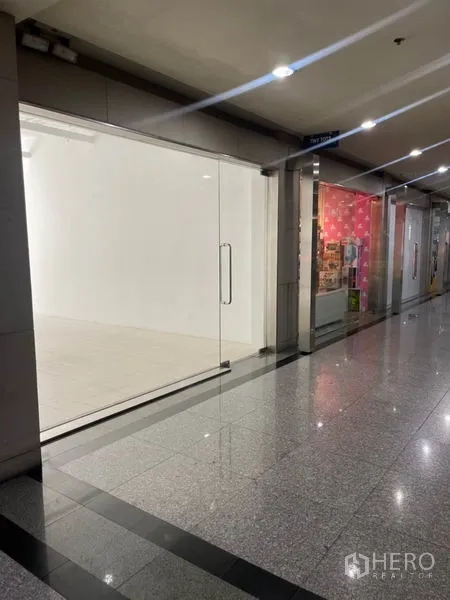 Retail Space for rent in Khlong Toei, Bangkok - Indoor mall corridor view of a vacant retail shop with full-height glass frontage.
