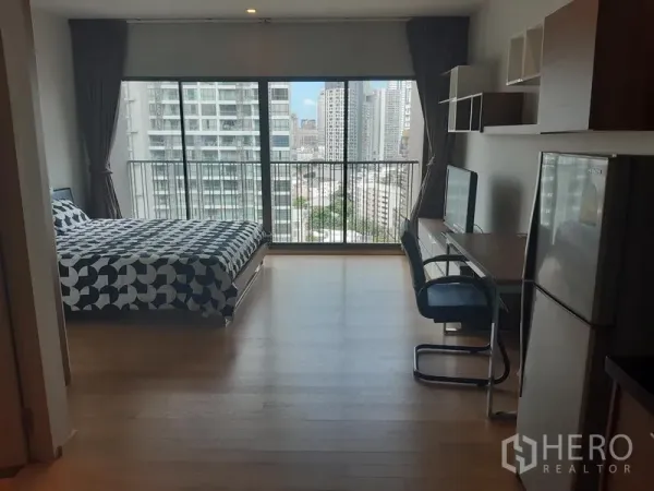 Condominium for rent in Bangkok - Bright studio condo with floor-to-ceiling windows, bed, desk and a city skyline view from the balcony.