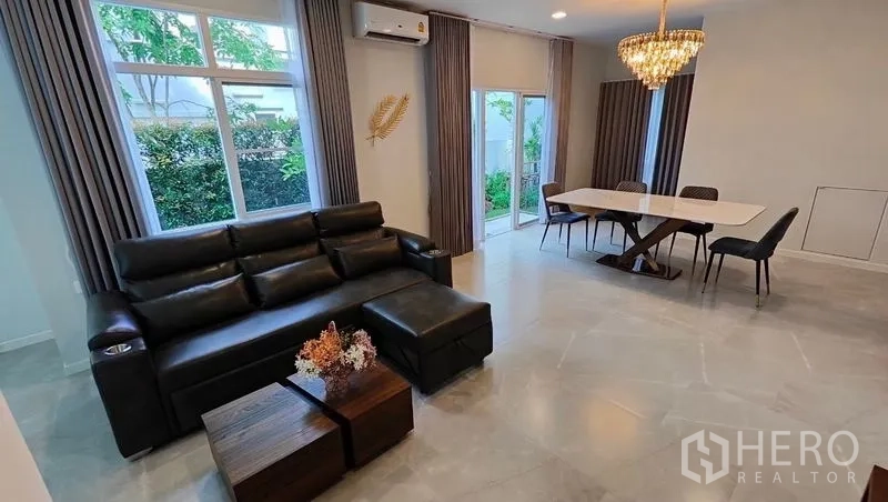 Detached House for rent in Prawet, Bangkok - Bright open-plan living and dining area with leather sofa, chandelier and sliding doors to the garden.