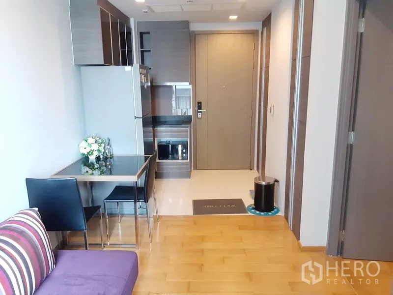 Condominium for sale in Khlong Toei, Bangkok - Compact kitchenette with built-in cabinets, fridge, microwave and a small dining set near the entry door.