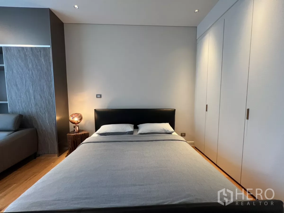 Condominium for rent in Pathum Wan, Bangkok - Minimal bedroom with upholstered bed, bedside lamp and white built-in closets.