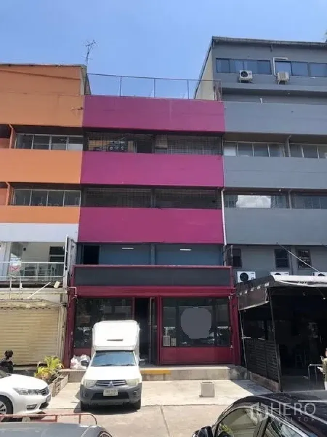 Shophouse for rent in Watthana, Bangkok - Four-storey shophouse exterior with bright magenta facade and front parking in the Ekkamai area.