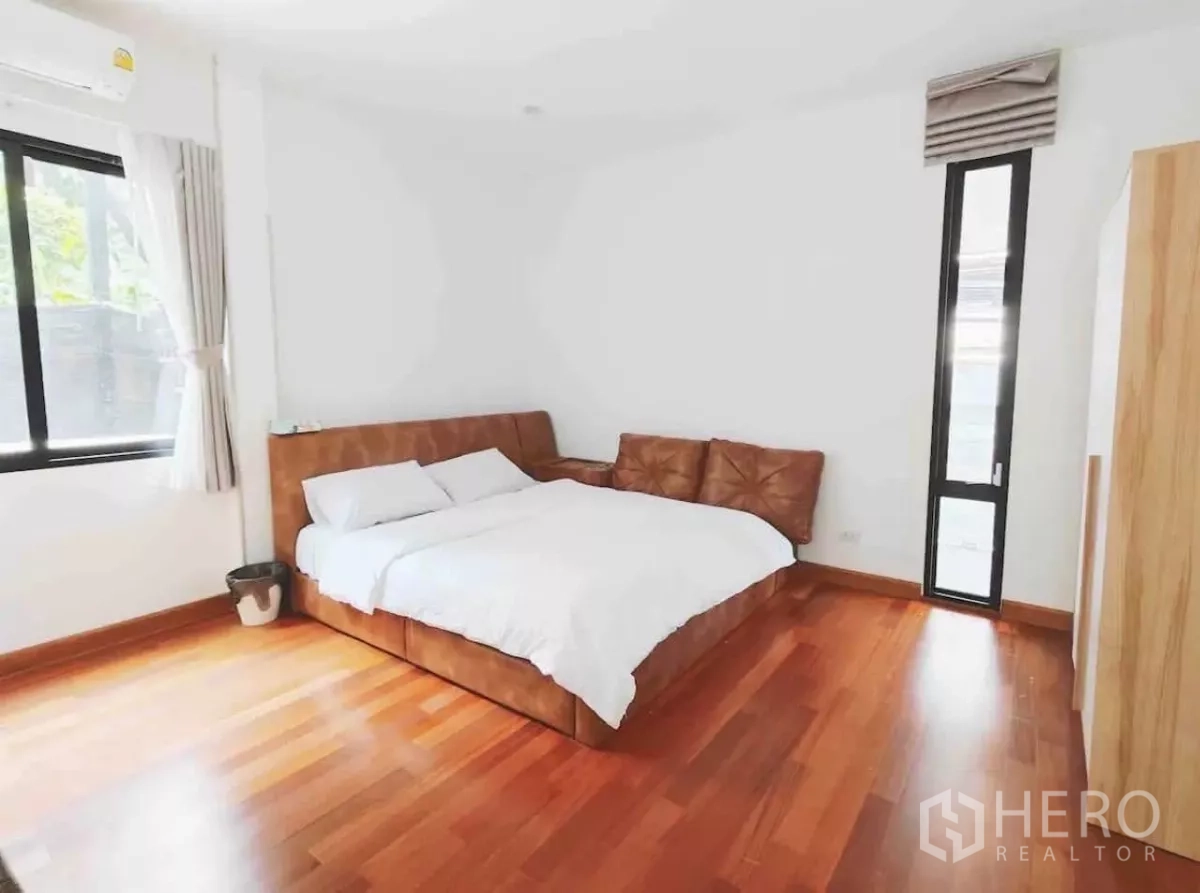 Detached House for rent in Phaya Thai, Bangkok - Cozy bedroom with brown leather bed, timber flooring and a tall narrow window.