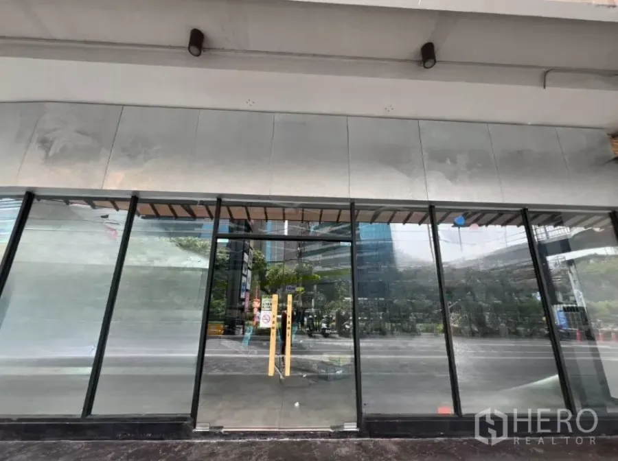 Retail Space for rent - Street-level retail storefront with full-height glass and double doors under a covered walkway, reflecting nearby city buildings.