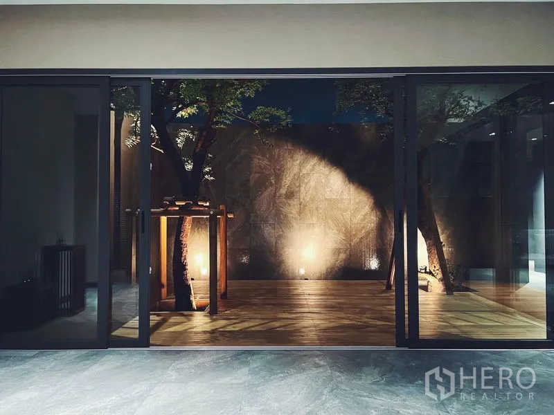Detached House for rent or sale in Bangkok - Night-lit courtyard deck with feature tree seen through sliding glass doors.
